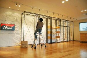 NANGA(ナンガ)滋賀本社ショールーム、雪山をイメージしたしわ加工の壁の前の置かれたシュラフ展示用什器のライティング調整